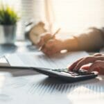 man uses a calculator while writing in tax forms