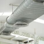 a silver, commercial air duct on the ceiling of a white office space