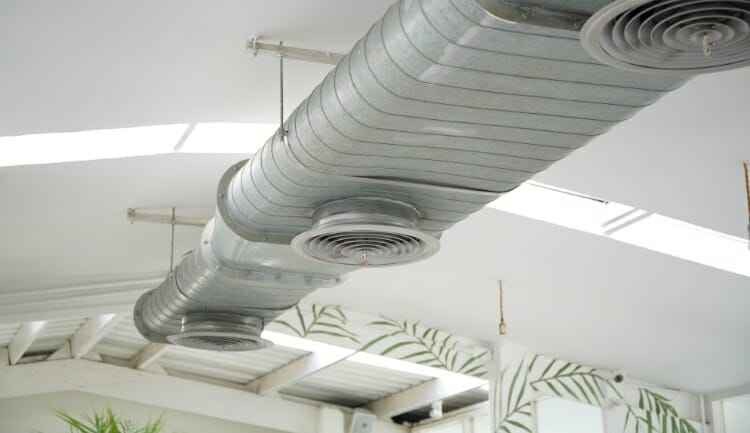 a silver, commercial air duct on the ceiling of a white office space