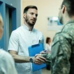 a doctor and a man in army digital camo shake hands in a hospital