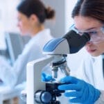 tech using microscope at pharmaceutical lab